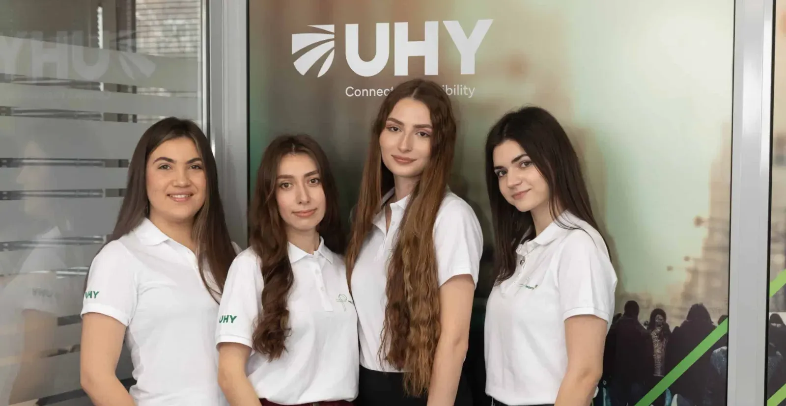Четверо співробітниць UHY Prostir у фірмових поло на тлі банера UHY