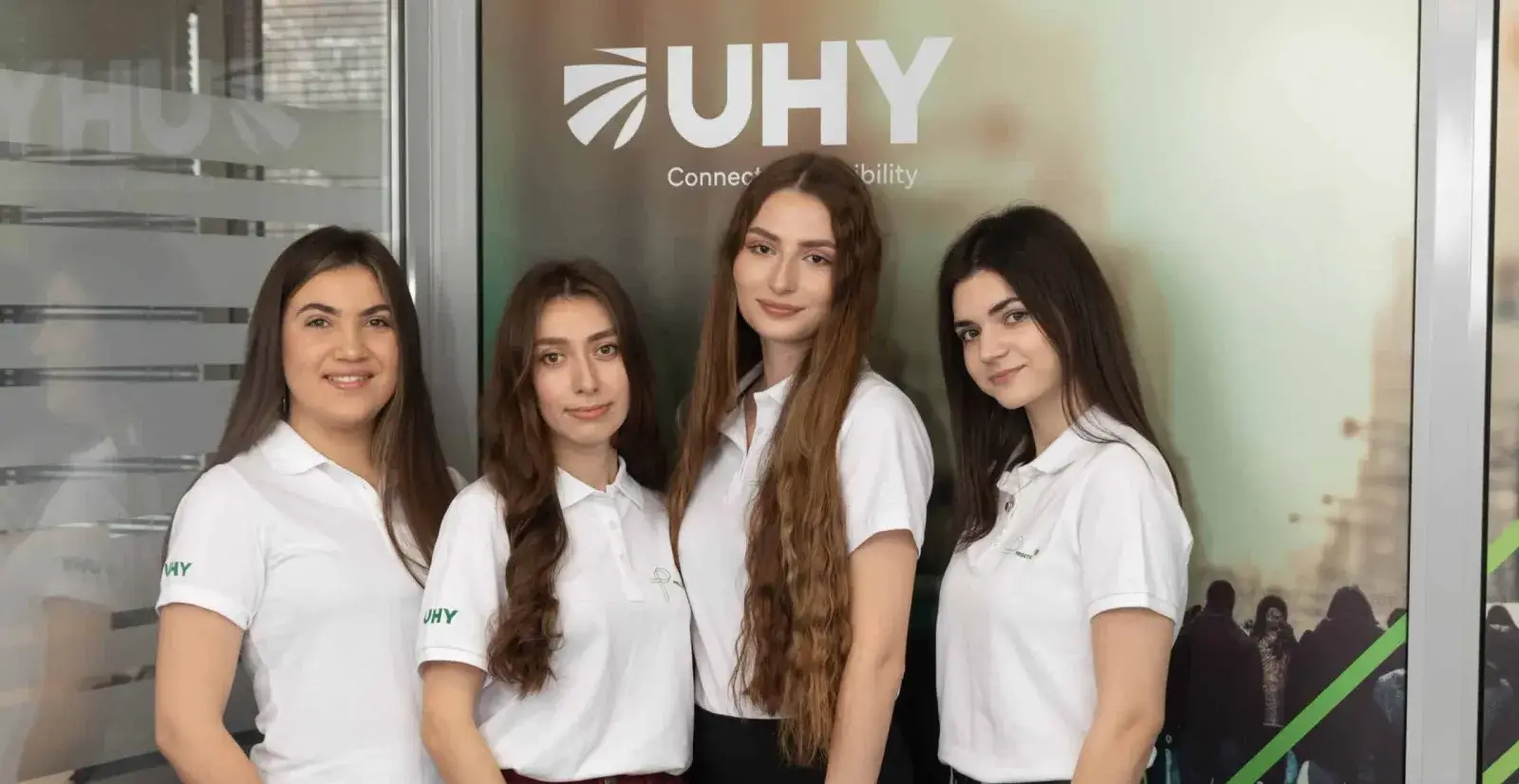 Четверо співробітниць UHY Prostir у фірмових поло на тлі банера UHY